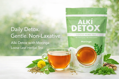 Alki Detox tea package with a cup of tea and tea leaves on a blurred green background